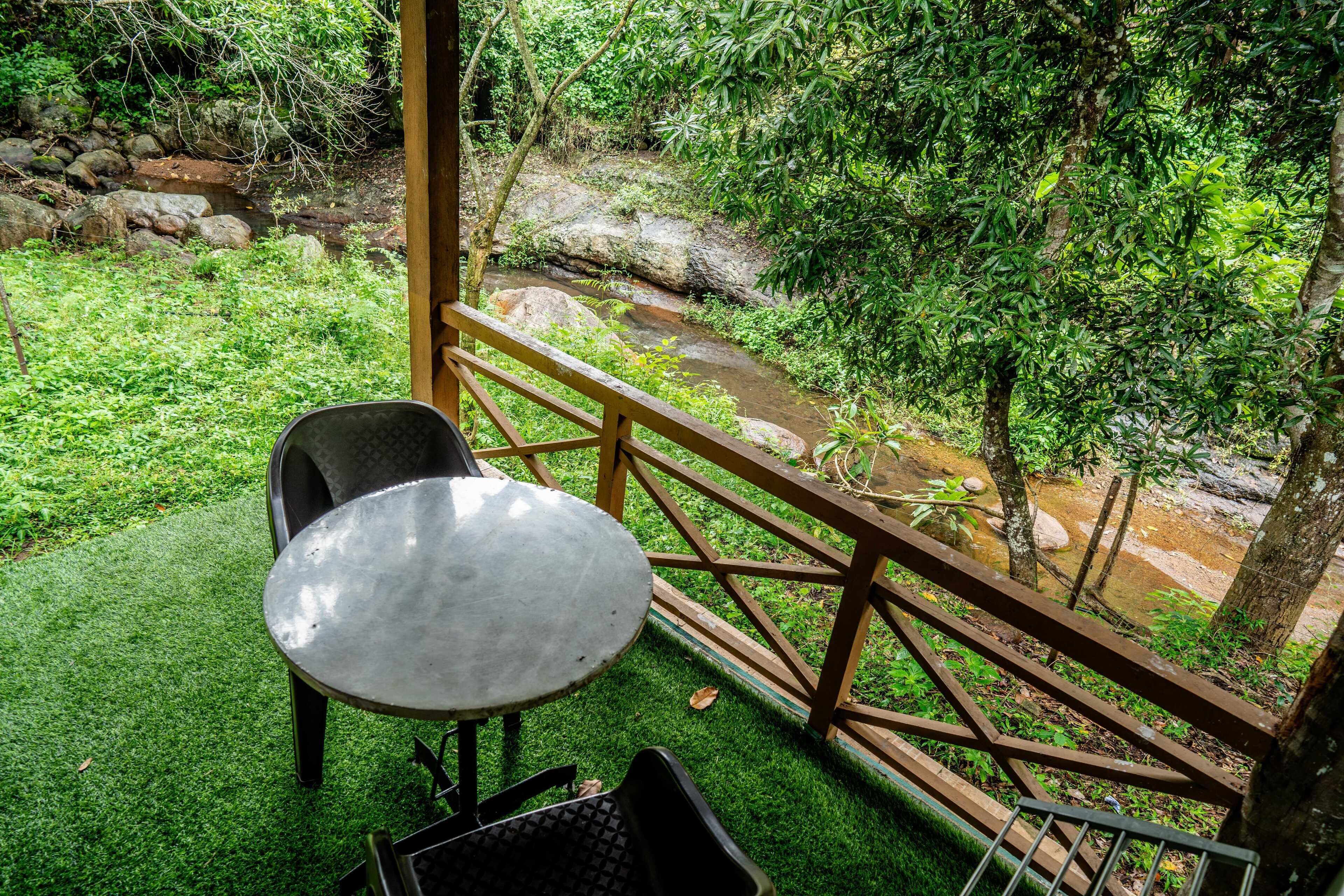 A balcony with a table and chairs overlooking a stream and lush greenery.
