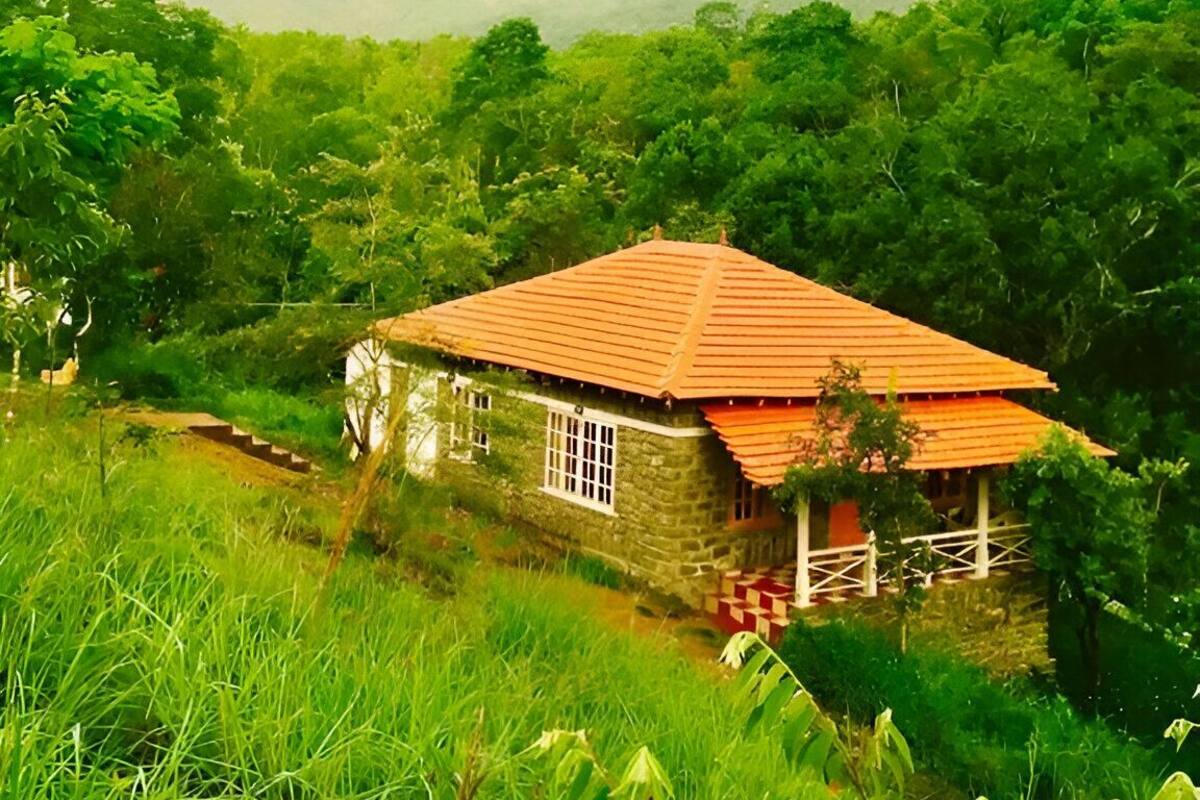Ein Haus aus Stein mit rotem Dach, umgeben von üppiger Vegetation und Hügeln im Hintergrund.