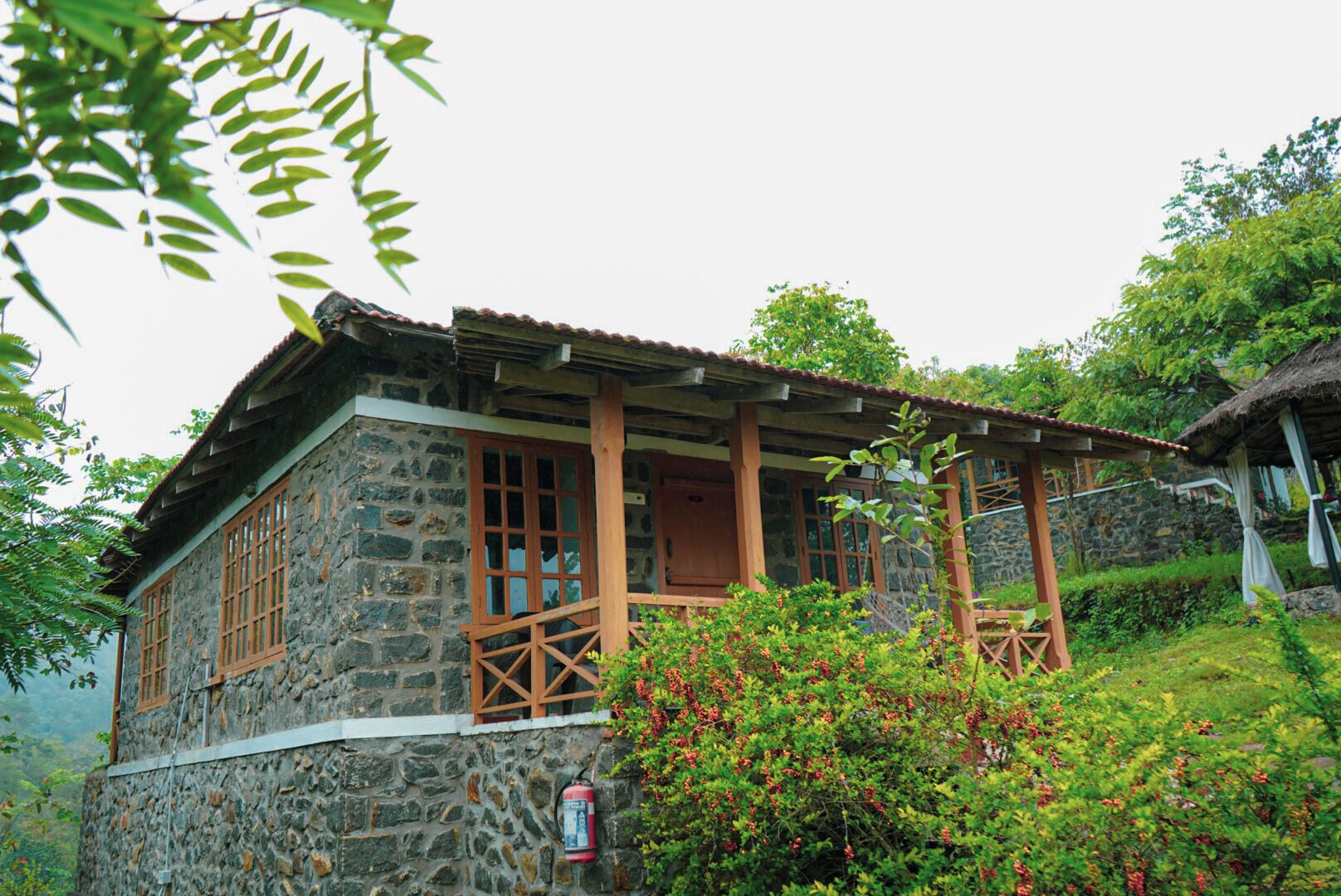 A stone building with wooden windows and a balcony, surrounded by greenery.