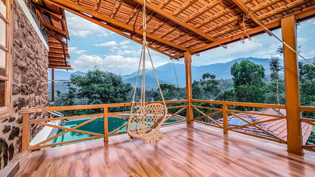 A wooden deck with a hanging chair overlooking a swimming pool and a mountainous landscape.
