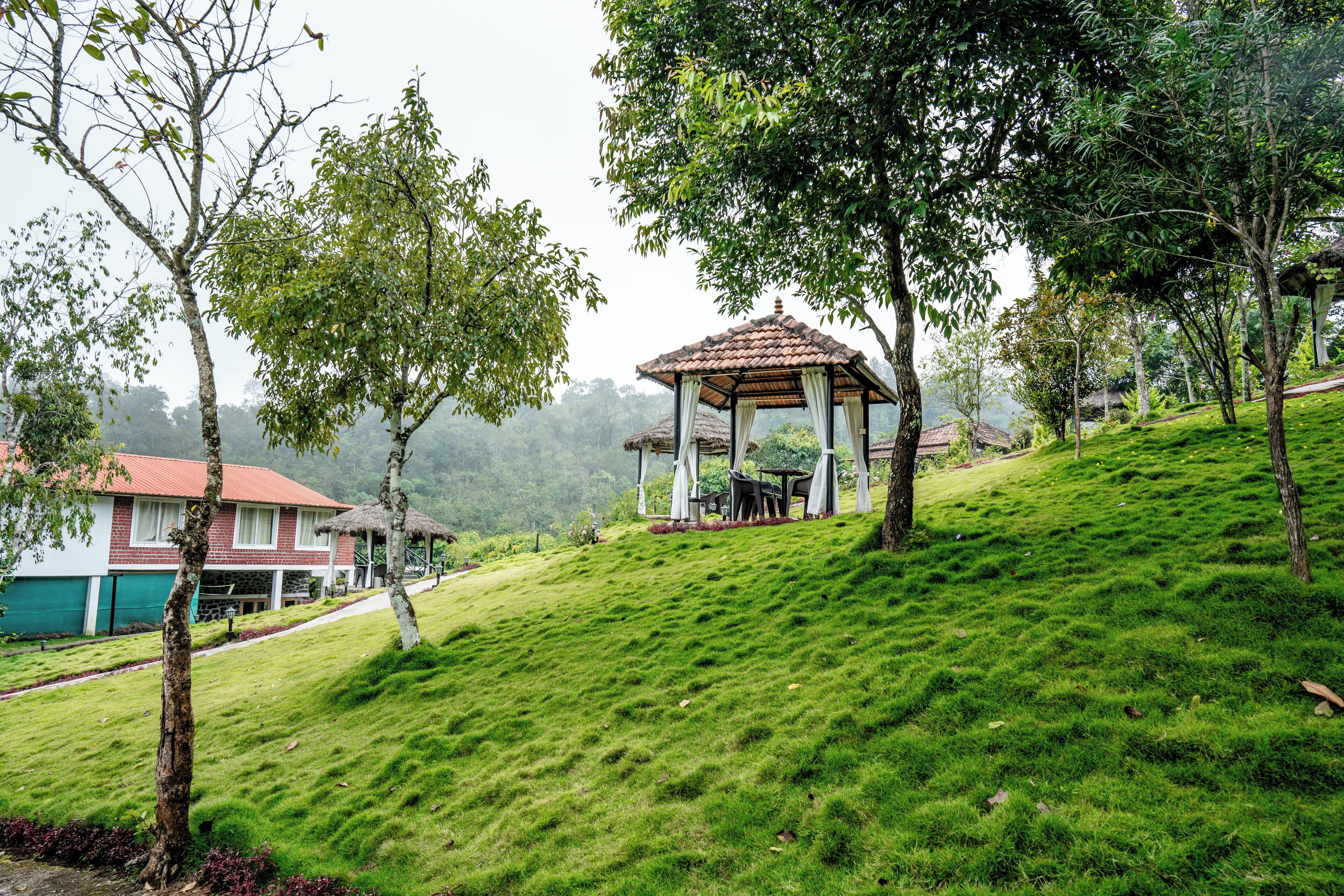 A gazebo on a grassy hill with a house in the background.