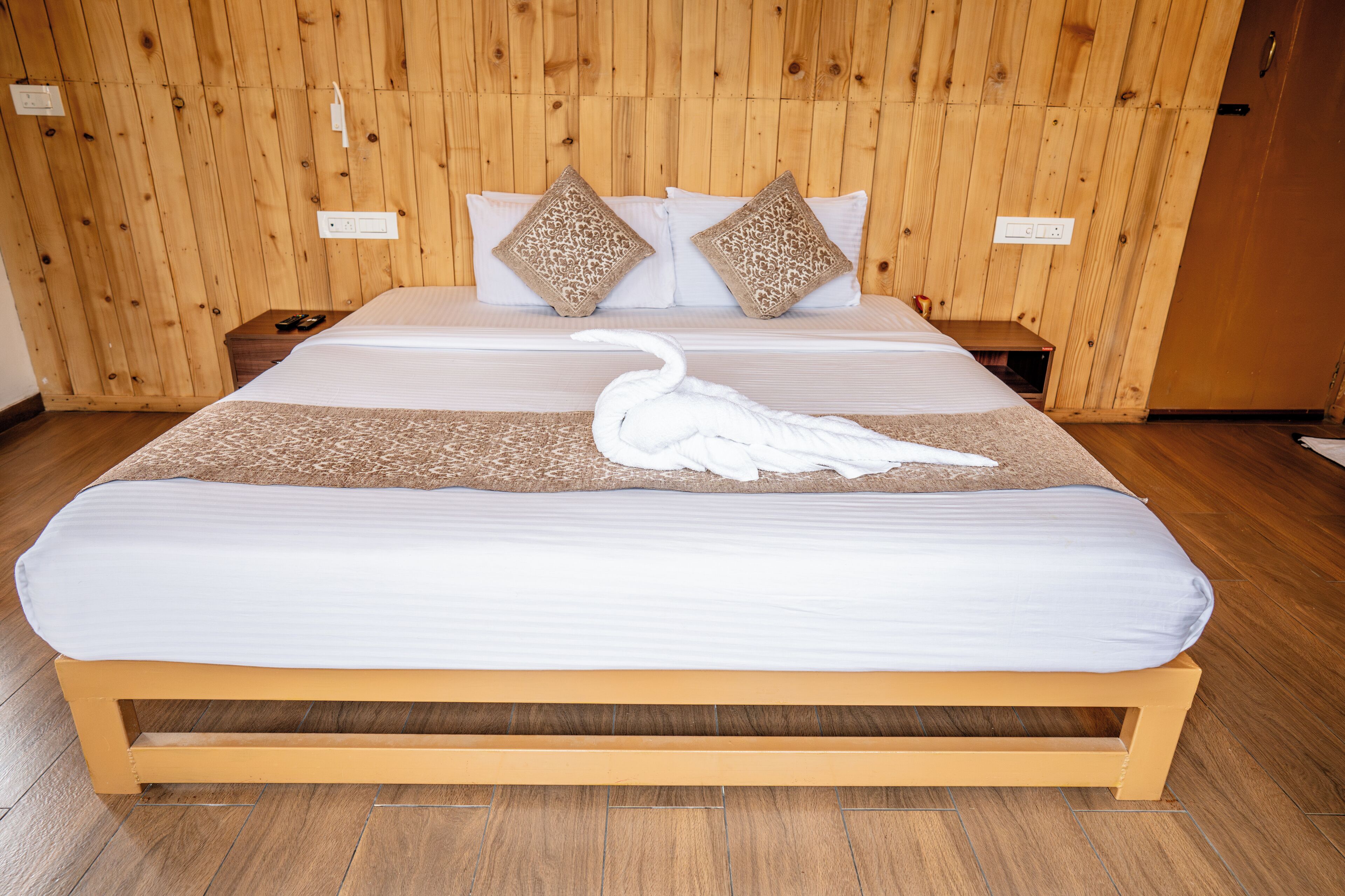 Un grand lit recouvert d’une couverture blanche et agrémenté d’un coussin décoratif en forme de cygne. La pièce est dotée de murs et d’un plancher en bois.