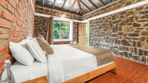 A bedroom with a stone wall, a wooden bed, and a window with a view of trees.