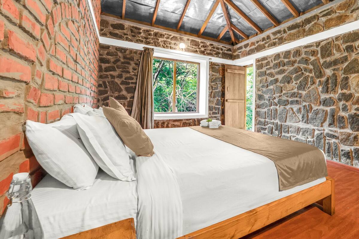 Ein Schlafzimmer mit Steinswand, einem Holzbett und einem Fenster mit Blick auf Bäume.
