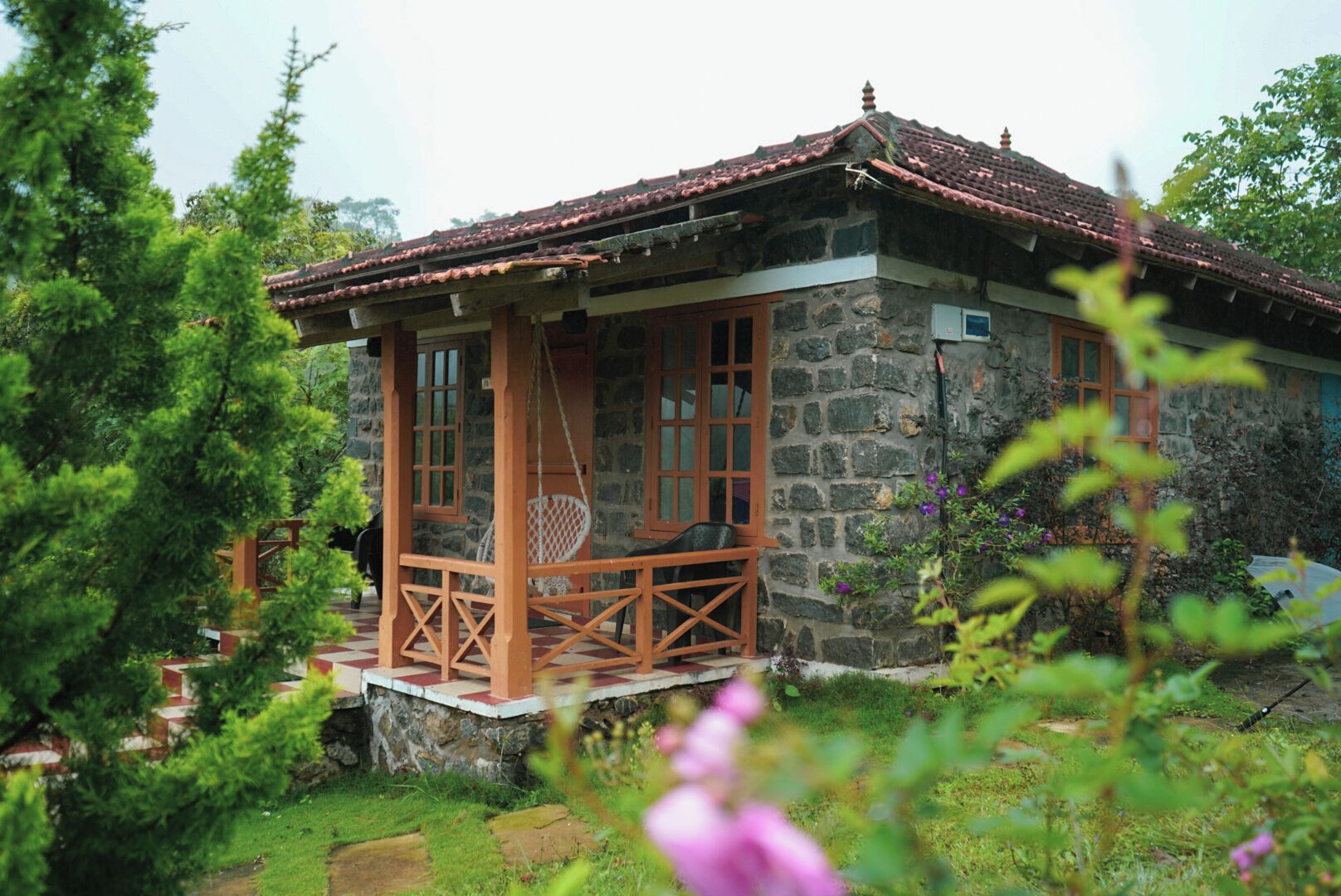 A stone building with a red-tiled roof, a wooden porch with a swing, and a small window.
