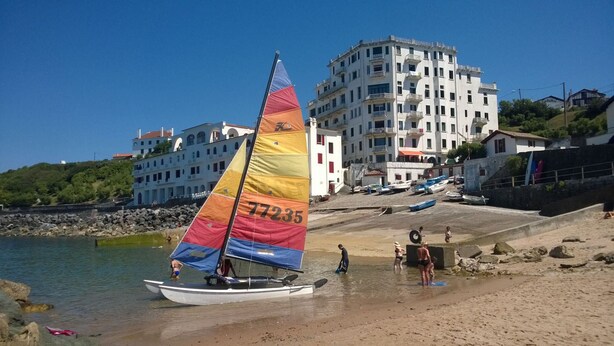 Une plage avec un voilier, des personnes et des bâtiments en arrière-plan.