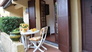 A patio with a table and chair, a potted plant, and a door leading to an interior space.
