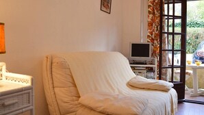 A cozy room with a single beige sofa, a small table with a television, and a window with curtains.