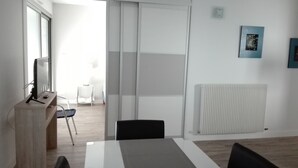 A modern office space with a large table, chairs, a computer, and a sliding door leading to another room. - Comfortable T2 near beach, 4 ppl, elevator (Les Sables-d'Olonne)