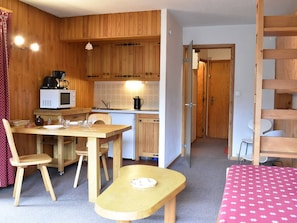 A compact kitchen with wooden cabinets, a microwave, and a sink. There is a dining table with chairs and a small bench. - Studio in Méribel - Near slopes, Parking, Pets allowed (Méribel)
