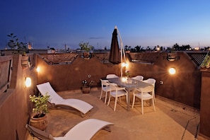 Una terraza exterior con una mesa y sillas, sillones de descanso y plantas en macetas.