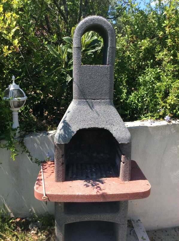 A stone-built outdoor oven with a handle on top, set against a backdrop of greenery and a white wall. - Beautiful new rental, 3 bedrooms, 400 m from beach and shops, absolute calm.75 m2 (Porticcio)