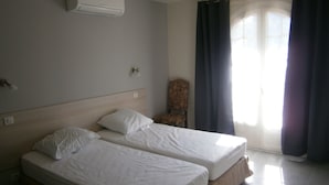 Ett hotellrum med två separata sängar, en stol och ett fönster med gardiner.