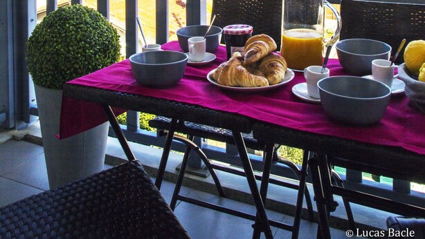 Un balcón con una mesa preparada para el desayuno, con vista a una playa y edificios.