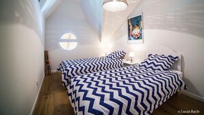 Un dormitorio con dos camas, un ventanal circular, una lámpara en el techo y un cuadro en la pared.
