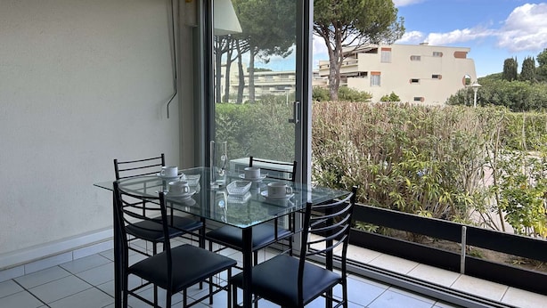 A balcony with a glass table and chairs, a yellow awning, and a view of buildings and trees. - Air-Conditioned Studio with Terrace, Pool & Parking - Sleeps 4, Steps from Port Camargue Beach (Port Camargue)