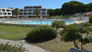 A swimming pool surrounded by a white fence, with a multi-story building in the background. - Air-Conditioned Studio with Terrace, Pool & Parking - Sleeps 4, Steps from Port Camargue Beach (Port Camargue)