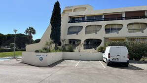 A modern building with a parking lot, a white van, and a sign indicating 'Garages' with an arrow pointing left. - Air-Conditioned Studio with Terrace, Pool & Parking - Sleeps 4, Steps from Port Camargue Beach (Port Camargue)