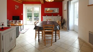 Uma sala de jantar com mesa e cadeiras de madeira, uma TV sobre um armário branco e uma parede vermelha.