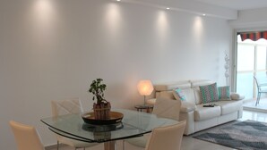 A modern living room with a glass dining table, white sofas, and a lamp.