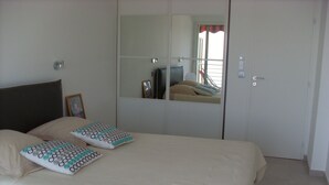 A bedroom with a bed, two pillows, a bedside table, a mirror, and a door.