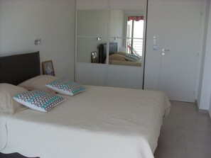 A bedroom with a bed, two pillows, a bedside table, a mirror, and a door.