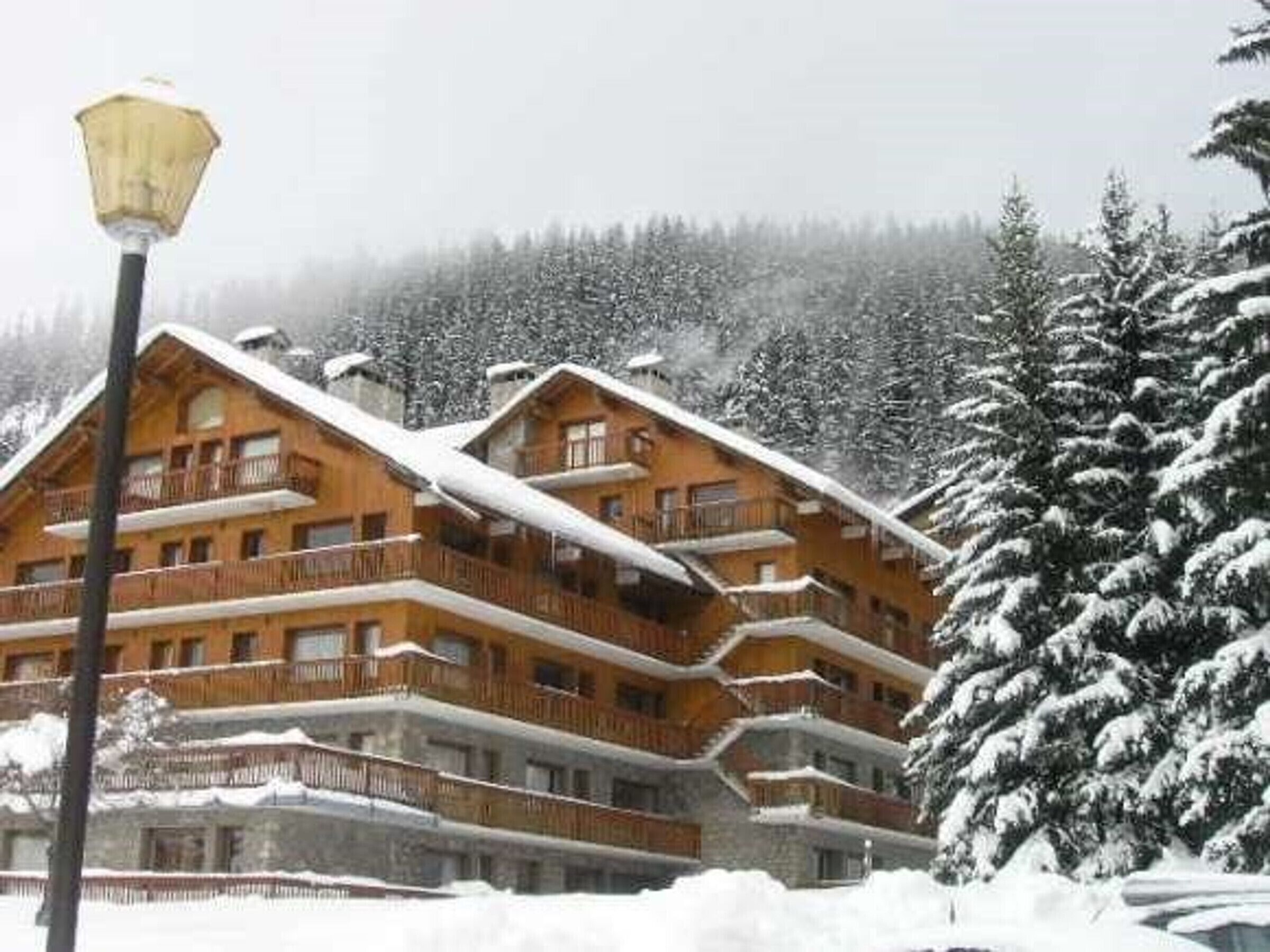 A multi-story wooden lodge with balconies, surrounded by snow-covered trees.