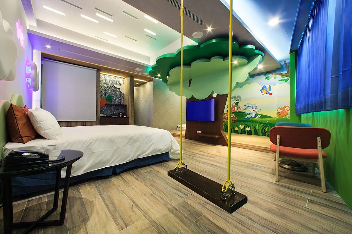 Una habitación de hotel moderna con cama, escritorio, silla, televisión y un mural en la pared.