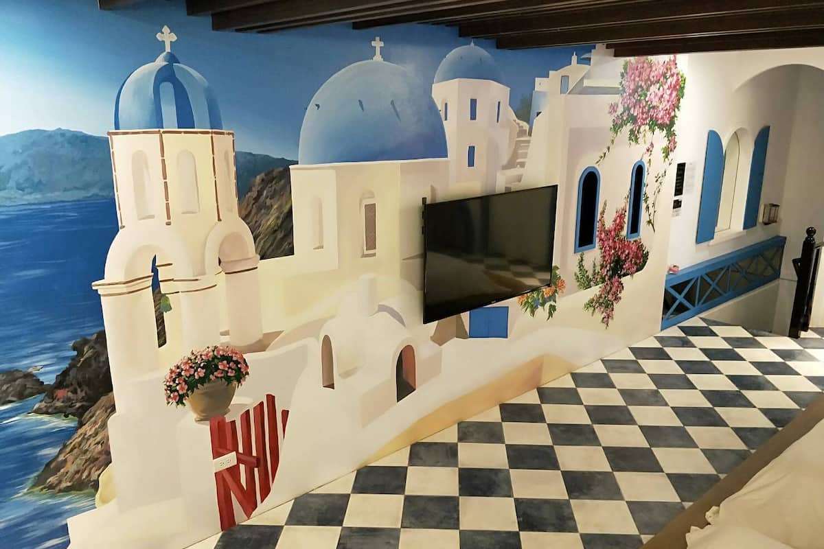 Una habitación con suelo a cuadros, un televisor de pantalla plana y un mural de edificios blancos con cúpulas azules.