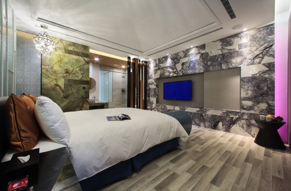 Una habitación de hotel moderna con una cama grande, un televisor montado en la pared y un revestimiento de mármol.