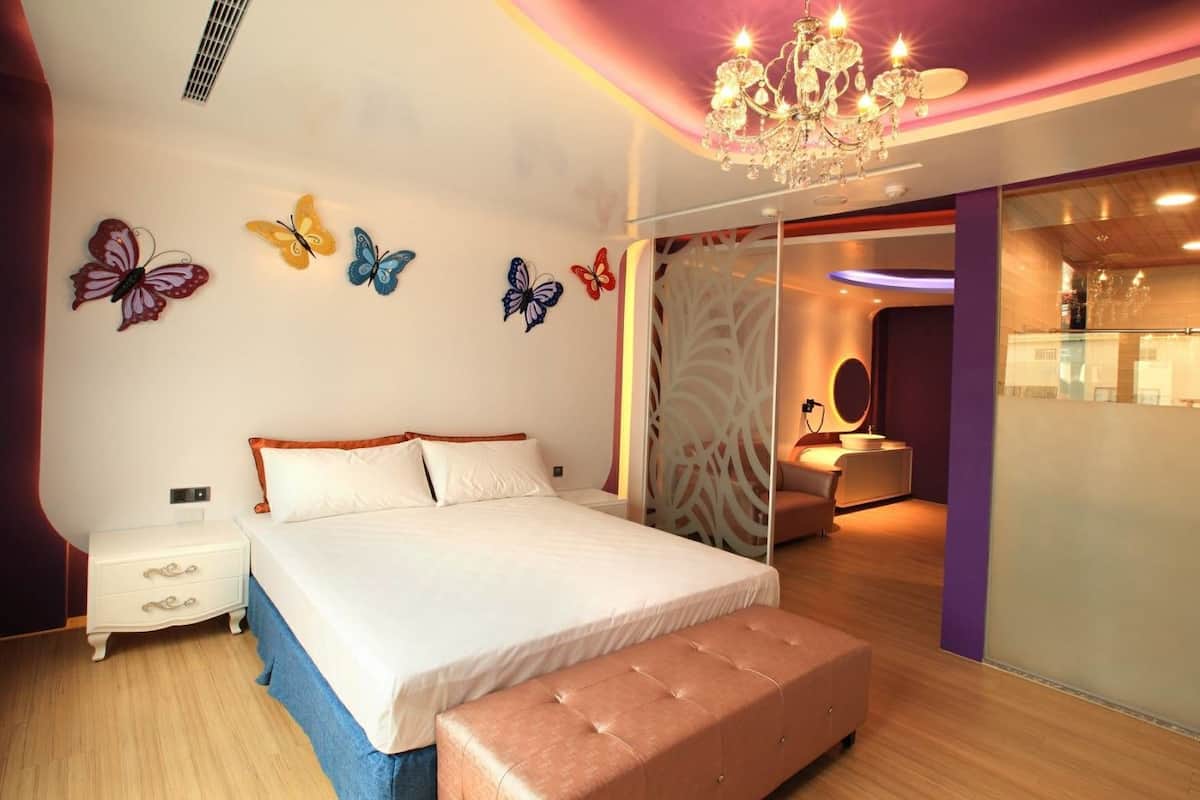 Un dormitorio moderno con una cama grande, una mesita de noche, un banco y un baño visible a través de una mampara de vidrio.