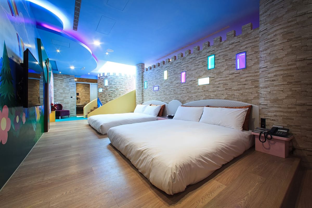Una habitación de hotel con dos camas, una pared de piedra, una escalera y un mural colorido.