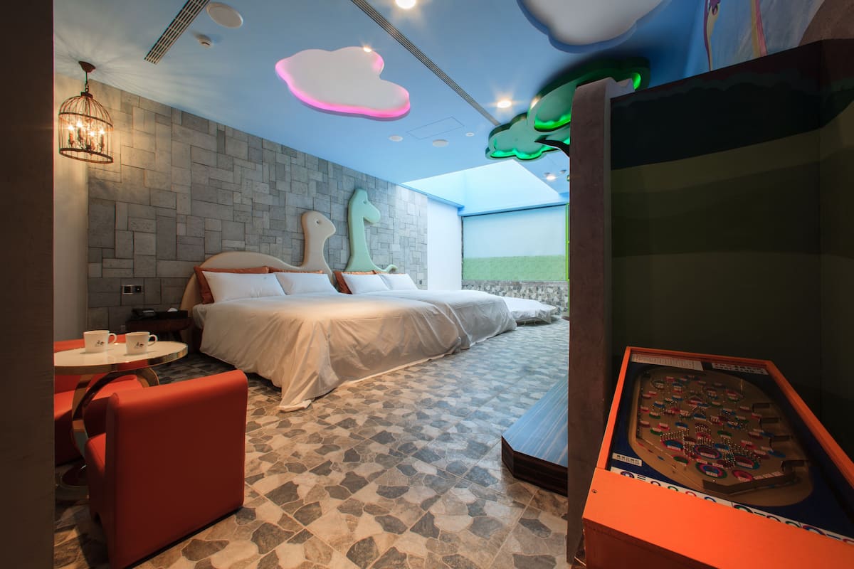 Habitación de hotel con cama, una mesita con dos tazas, una silla roja y un amplio ventanal con vistas.