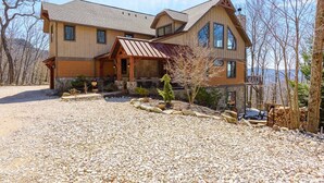A large, two-story house with a stone foundation, a covered porch, and a mountain view.