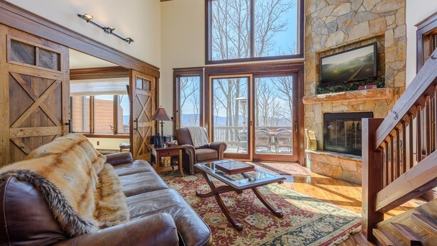 A spacious living room with a stone fireplace, large windows, and a cozy leather couch.