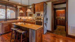 A kitchen with wooden cabinets, a granite island with stools, stainless steel appliances, and pendant lighting.