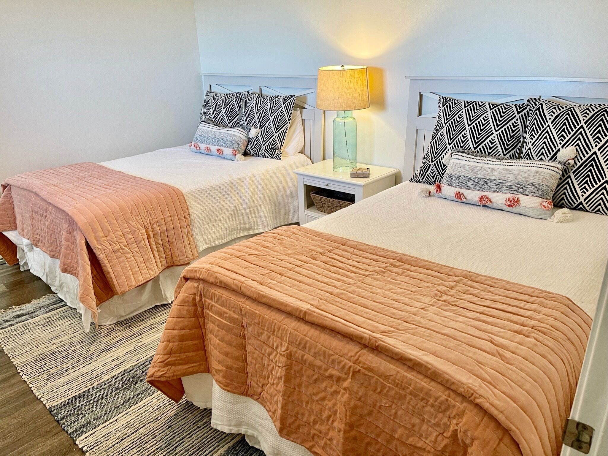 A hotel room with two beds, each with patterned pillows and a bedside table with a lamp.