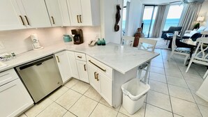 Una cocina moderna con armarios blancos, lavavajillas y una pequeña isla con un cubo de basura.