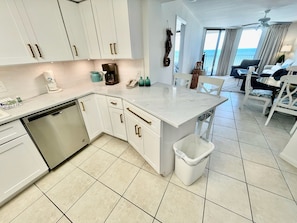 A modern kitchen with white cabinets, a dishwasher, and a small island with a trash bin.