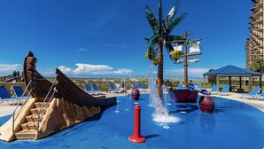 Un área de piscina con un parque acuático, sillas de descanso y una palmera.