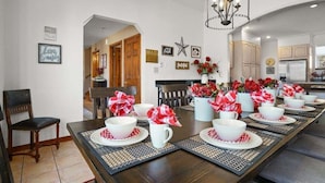 Comedor con una larga mesa dispuesta para una comida, con tazones y tazas blancos y servilletas rojas.