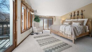 Un dormitorio con una cama grande, una silla, un ventanal y una planta.