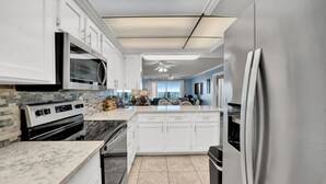 Una cocina moderna con armarios blancos, encimera de granito, horno empotrado y refrigerador de acero inoxidable.
