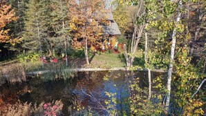 A serene pond with a wooden dock, surrounded by autumn foliage and a rustic house in the background. - The Trail's Edge / "Captain's Quarters" Is A Gorgeous Retreat, In Any Season.  (Duluth)