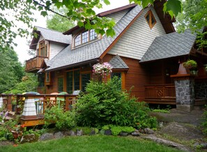 A wooden cabin with a stone porch, a covered deck, and a garden area with rocks and plants. - The Trail's Edge / "Captain's Quarters" Is A Gorgeous Retreat, In Any Season. (Duluth)