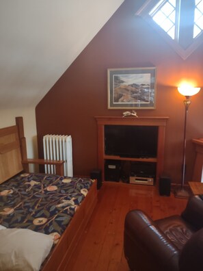 A bedroom with a bed, a wooden headboard, a radiator, a fireplace, a television, and a lamp. - The Trail's Edge / "Captain's Quarters" Is A Gorgeous Retreat, In Any Season. (Duluth)