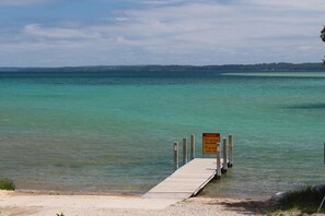 A wooden pier extending into a body of water with a warning sign about shallow water and no diving.