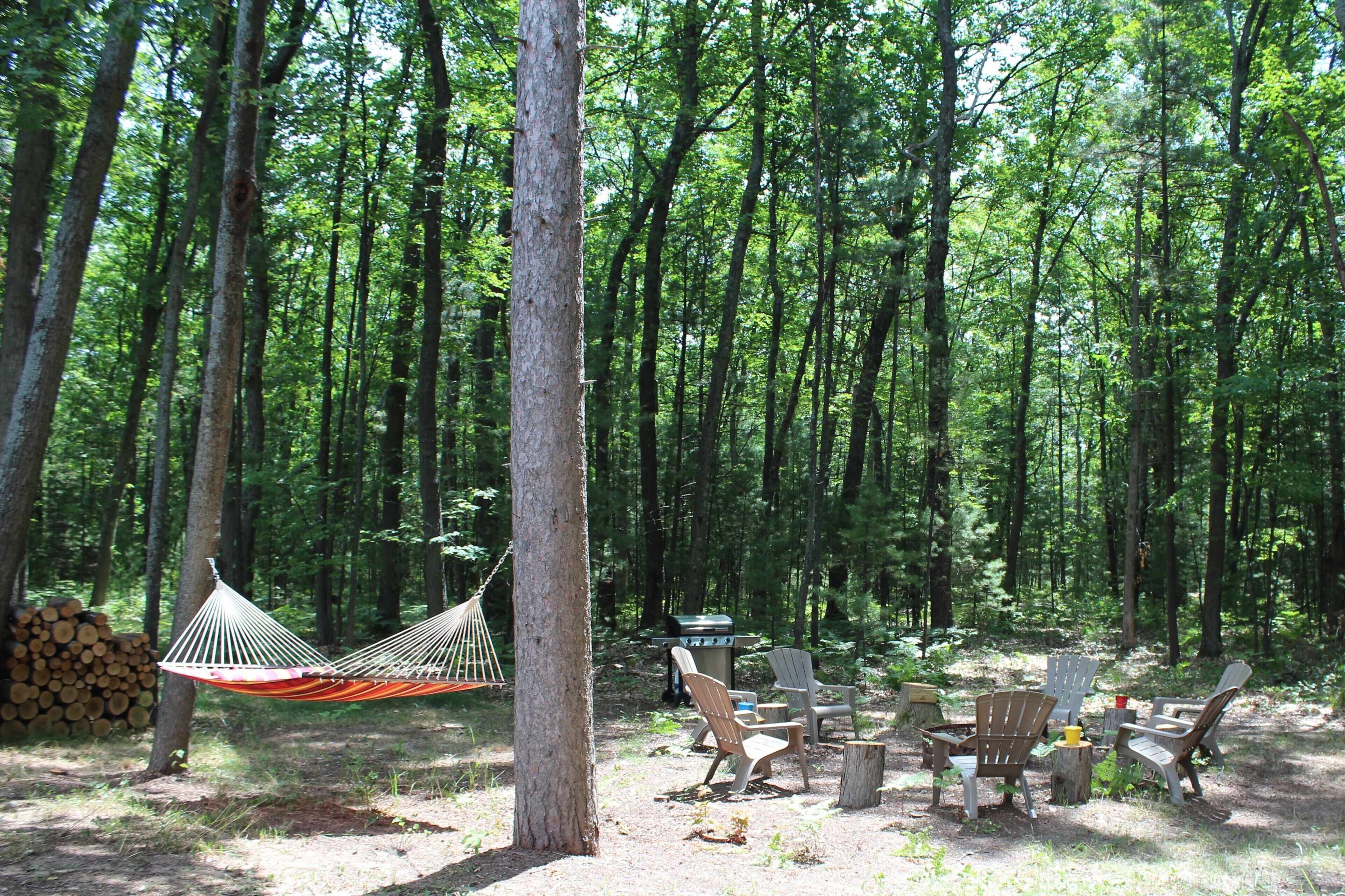 A hammock, outdoor chairs, and a grill in a forest setting.
