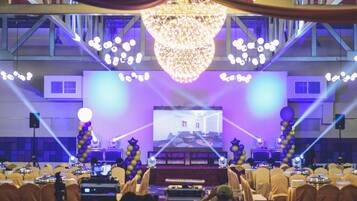 A conference room with a stage, rows of chairs, and a large chandelier.