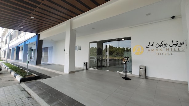 Het exterieur van Aman Hills Hotel, met een modern ontwerp, toont een ruime entree met glazen deuren en een naamplaatje.